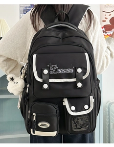 Detail of black multi-pocket backpack with white piping and plush bear accessory