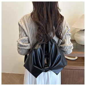 Back view of a black oversized bow-shaped backpack in matte leather on a person