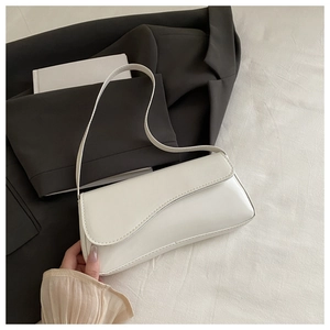 Close-up of a white patent leather baguette bag with a stylish wavy flap on dark fabric