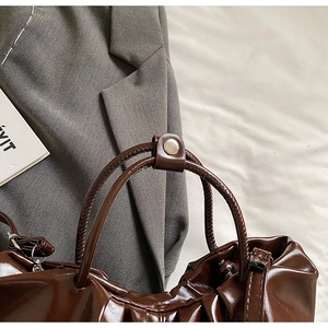 Detail der dunkelbraunen Falten-Cloud-Tasche mit Glanzeffekt und Golddruckknopf