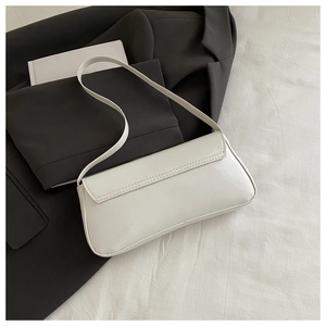 Detail of white patent leather baguette bag featuring clean stitching and minimalist flap