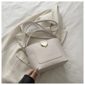 Gros plan du sac seau crème avec cuir texturé litchi et boucle coeur dorée élégante