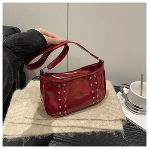 Detail of dark red patent leather crossbody bag with silver rivet studs and wide strap