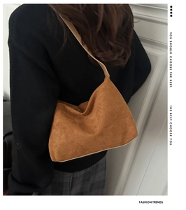Brown matte suede shoulder bag shown as a crossbody tote on model with black sweater