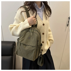 Olive green lightweight nylon backpack detail featuring a round metallic logo on the front