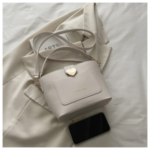 Détail du sac seau crème avec texture litchi et fermoir cœur doré sur la poche avant