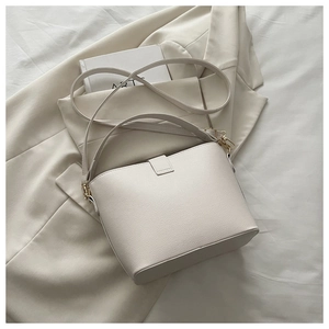 Gros plan du sac seau beige en cuir grainé avec détails de crochets dorés fins