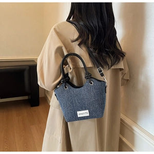 Dettaglio della borsa a secchiello in denim blu con manico in pelle nera indossata da un modello
