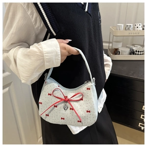 Détail d'un sac à main bleu clair avec grand nœud rouge, pois et pendentif en forme de cœur
