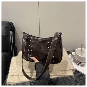 Macro shot of dark brown glossy underarm bag with silver rivets and wide strap