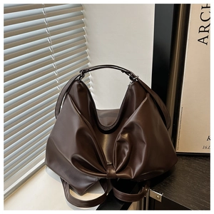 Detail of dark brown tote bag featuring a large bow design and textured faux leather surface