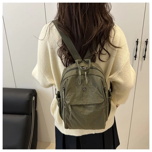 Close-up of olive green mini nylon backpack featuring front zip pocket and metal logo