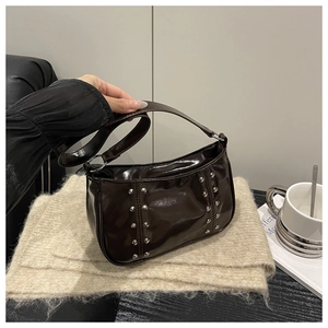 Detail of dark brown patent leather crescent bag with silver rivets on knit background