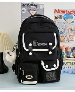 Detail of black multi-pocket school backpack with white piping and plush bear pendant