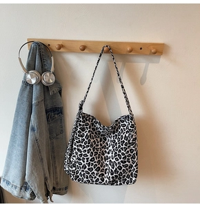 Detail of a large leopard print canvas tote bag hanging on a wooden rack with accessories
