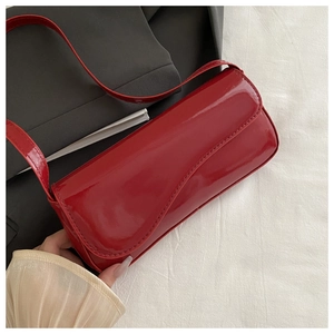 Detail of glossy red patent leather shoulder bag with sleek curved flap and thin strap