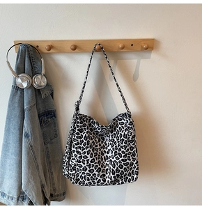 Detail of leopard print canvas tote bag hanging on a wooden hook with stylish accessories