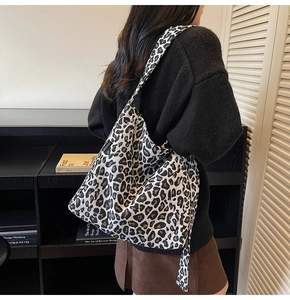 Detail of a large leopard print tote bag with a fashion label, worn as a crossbody bag