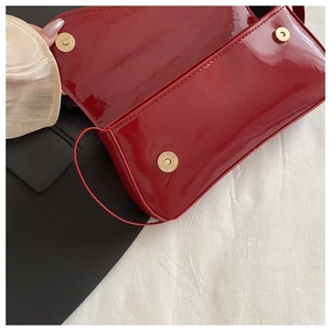 Close-up of glossy red patent leather handbag featuring dual gold magnetic closures