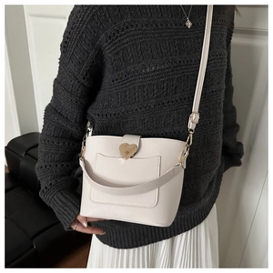 Détail du sac seau crème avec fermoir coeur doré porté sur un pull en maille