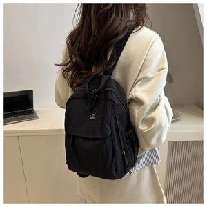 Detail of minimalist black nylon backpack showing rear view and slim straps on a model