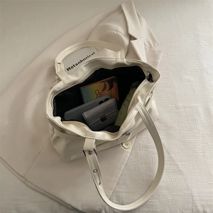 Minimalist beige patent leather tote bag with adjustable strap on a stylish white suit