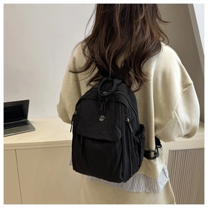 Detail of a minimalist black nylon backpack with a metal logo on the back of a model