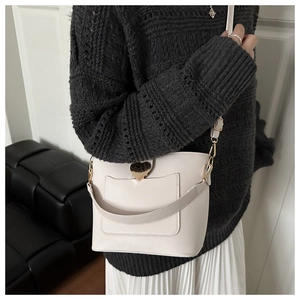 Détail d'un sac seau blanc crème avec fermoir coeur doré sur un pull en maille gris foncé