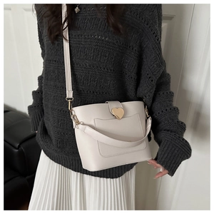 Fashionable cream bucket bag with golden heart clasp and wide strap on chic model