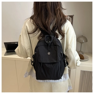 Detail of black nylon backpack featuring a metallic M logo on casual model outfit
