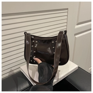 Detail of dark brown glossy baguette bag with silver studs on art book background