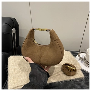 Close-up of brown suede crescent bag with gold hardware in cozy lifestyle setting
