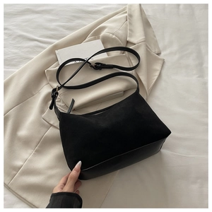 Close-up of black suede and smooth leather patchwork underarm bag on a chic white blazer