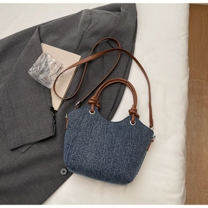 Dettaglio della borsa tote in denim blu con manici annodati in pelle marrone e dettagli