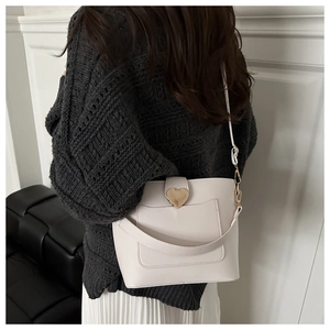 Detail of cream bucket bag with golden heart clasp and pebbled leather texture