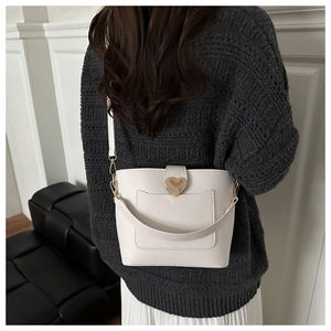 Chic cream bucket bag with gold heart clasp shown on a model in a minimal setting