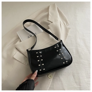 Detail of black glossy hobo bag with silver studs on a stylish cream blazer