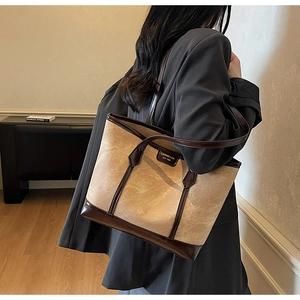 Détail latéral d'un grand sac cabas camel porté avec un tailleur gris sophistiqué