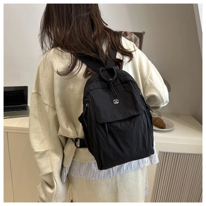 Close-up of minimalist black nylon mini backpack with silver metal logo M badge on cover