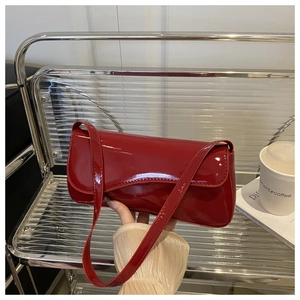 Close-up of a red patent leather shoulder bag held by a model in a trendy urban setting