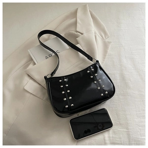 Detail of black patent leather half-moon bag featuring silver studs on a blazer