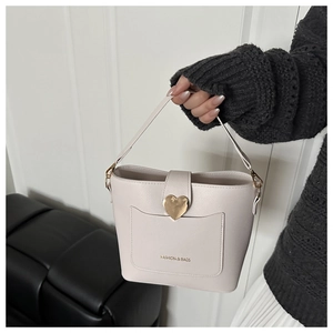 Gros plan détaillé d'un sac seau beige avec boucle cœur dorée et texture cuir grainé