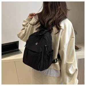 Modern black nylon backpack with metal M logo shown in a casual lifestyle setting