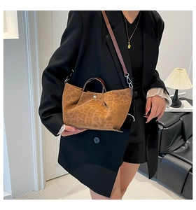 Detail of leopard print suede handbag featuring brown leather handles and metal snap closure