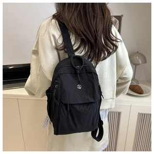 Detail of black nylon backpack with metal M logo shown on a model in a minimalist room