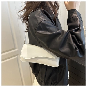 Detail of white patent leather shoulder bag with wavy flap edge on model in black jacket
