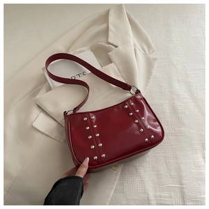 Close-up of burgundy shoulder bag with silver studs on a white blazer background