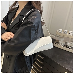Close-up of a white patent leather shoulder bag with a unique asymmetric curved flap