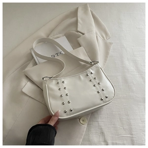 Detail of a creamy white half-moon underarm bag with silver rivets on a beige blazer