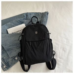 Detailed close-up of a black nylon backpack featuring a metallic M logo and zipper pockets